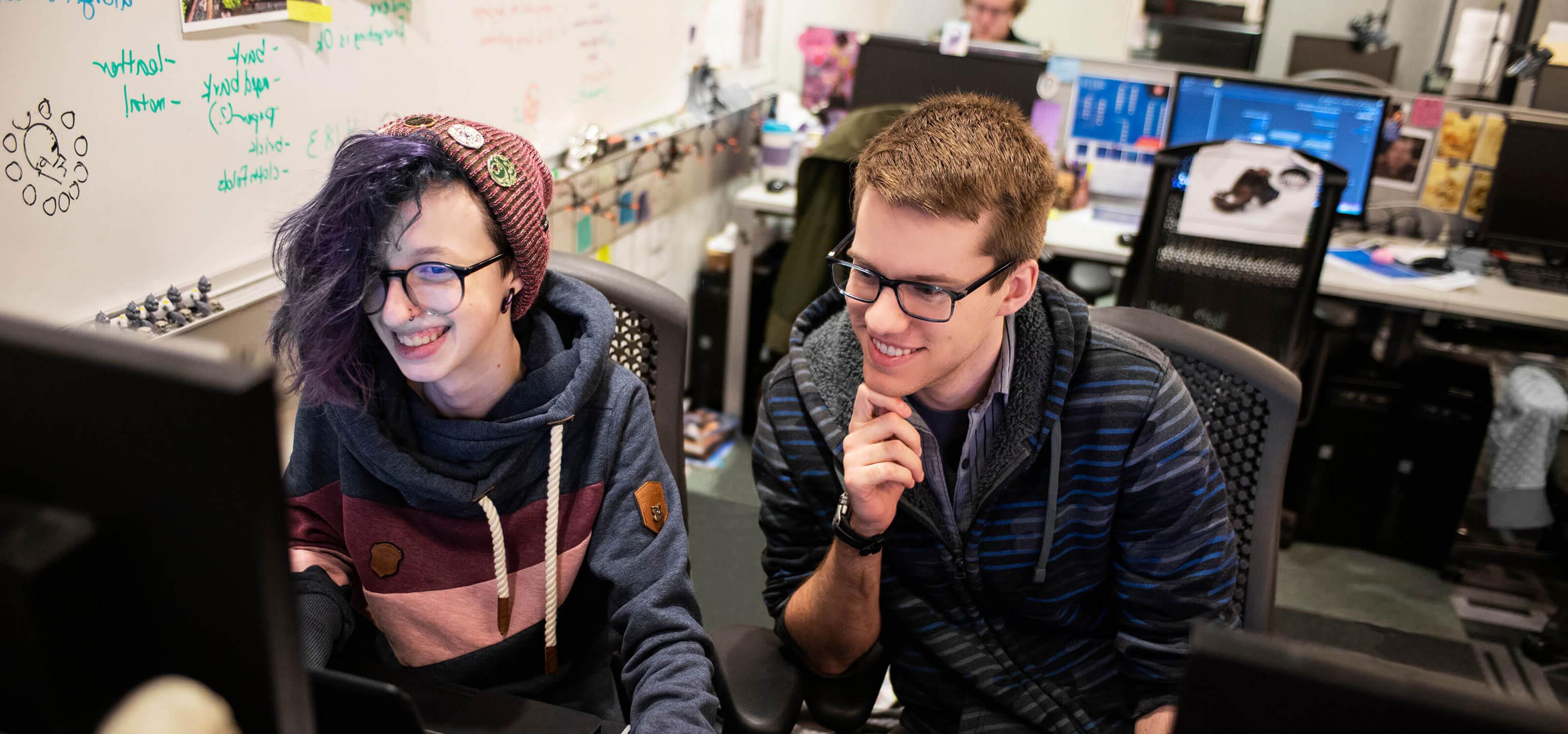 两个学生在计算机实验室一起工作，看着电脑显示器，微笑着.