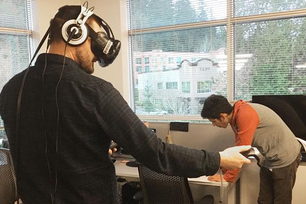 一名戴着VR头显的男子站在教室里，拿着两个游戏控制器，向左边做手势.
