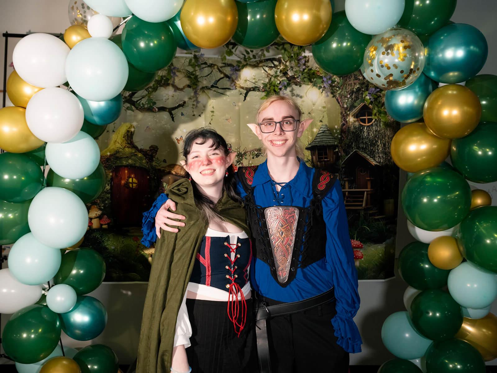 Two DigiPen students dressed as elves pose in front of a balloon arch at the first annual DigiProm.