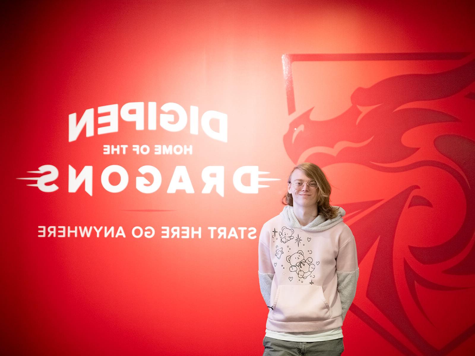 Student Tetra Chaney poses in front of a red wall with DigiPen’s Dragon logo on it and the words, “DigiPen龙之家-从这里开始到任何地方.”