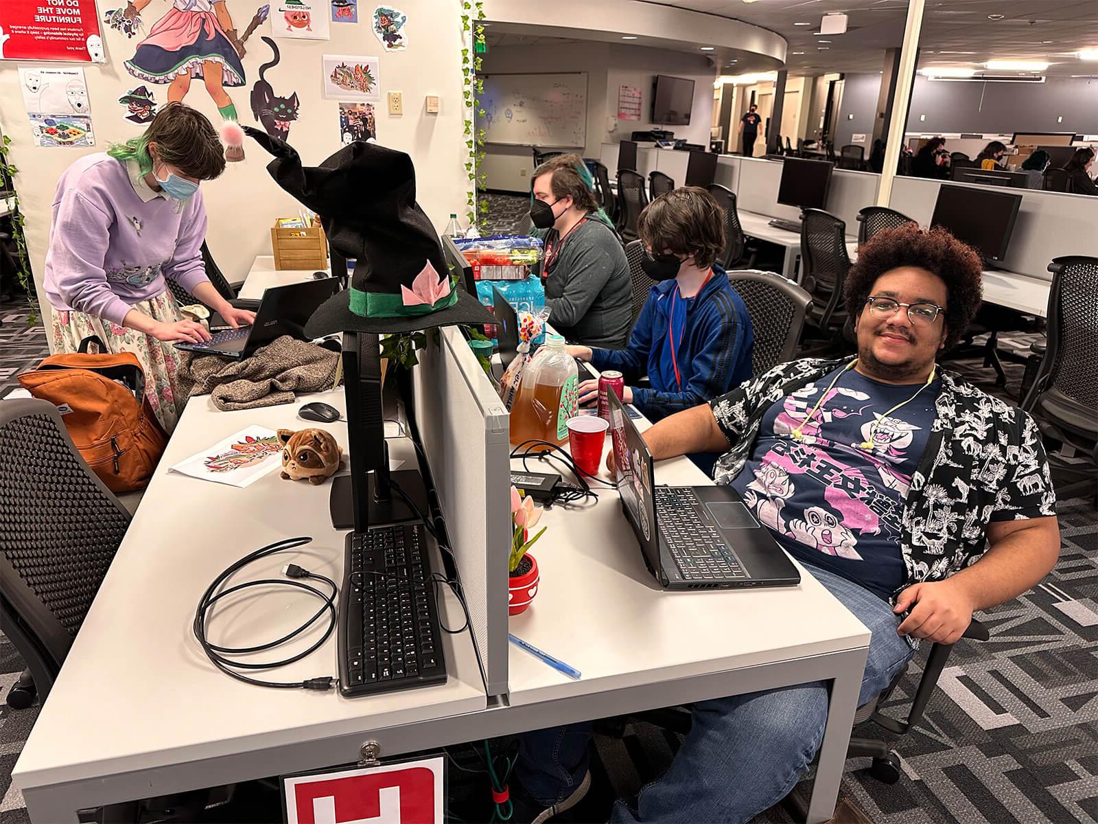 DigiPen students surrounded by snacks work on their Global Game Jam projects, one smiling for the camera.