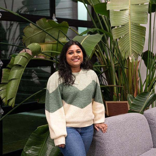 DigiPen的毕业生Neha Chintala站在沙发和一些高大的绿叶植物旁边微笑着.